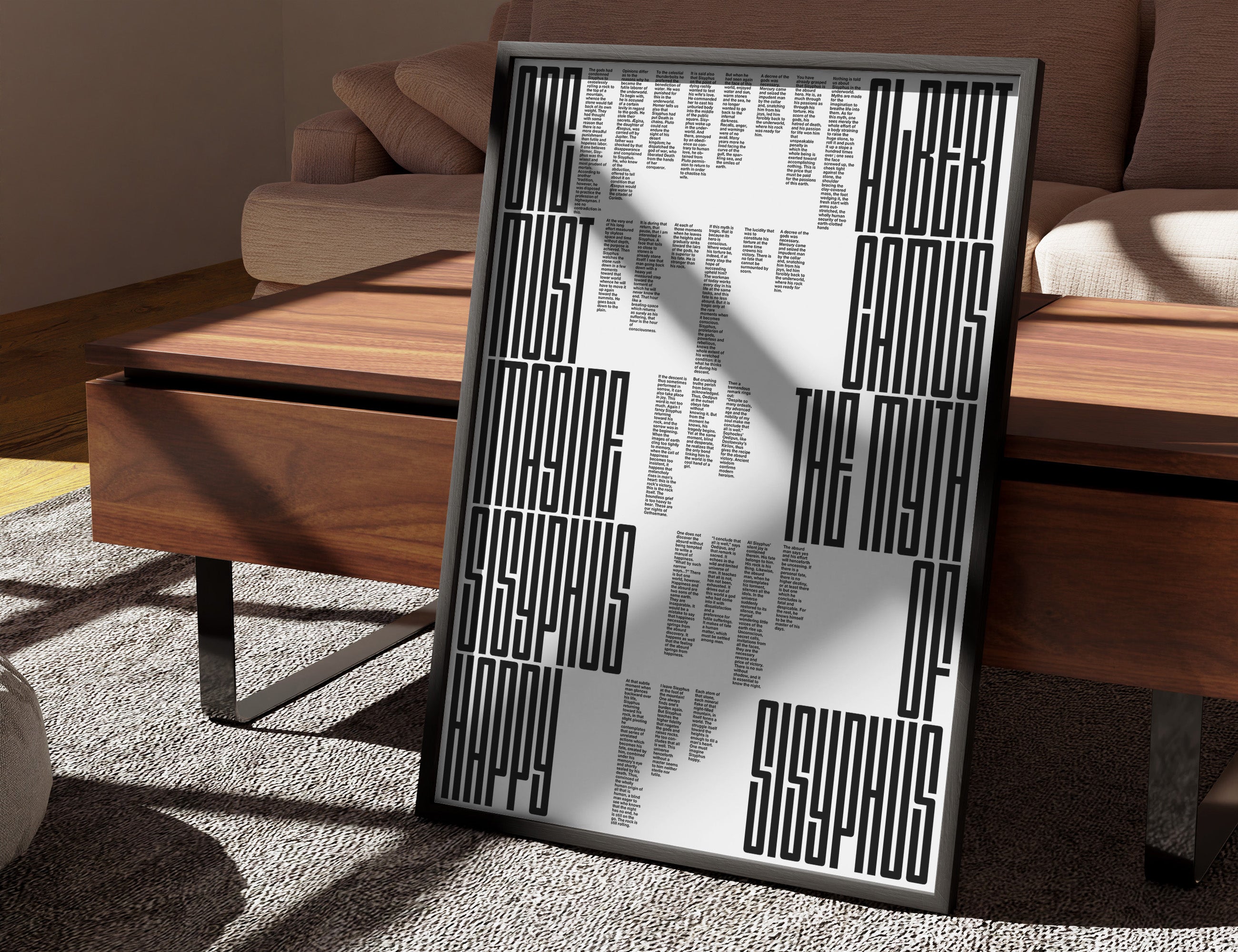 A framed the myth of sisyphus poster print featuring black and white geometric maze-like patterns and text, leaning against a wooden coffee table in a modern living room setting.